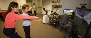 Associate Professor Sun Joo (Grace) Ahn, left, helps nine-year-old Maddie Lacey of Watkinsville, Ga., interact with the virtual buddy fitness kiosk in the Games and Virtual Environments Lab at Grady College, while Maddie’s mother, Cara Lacey, looks on.