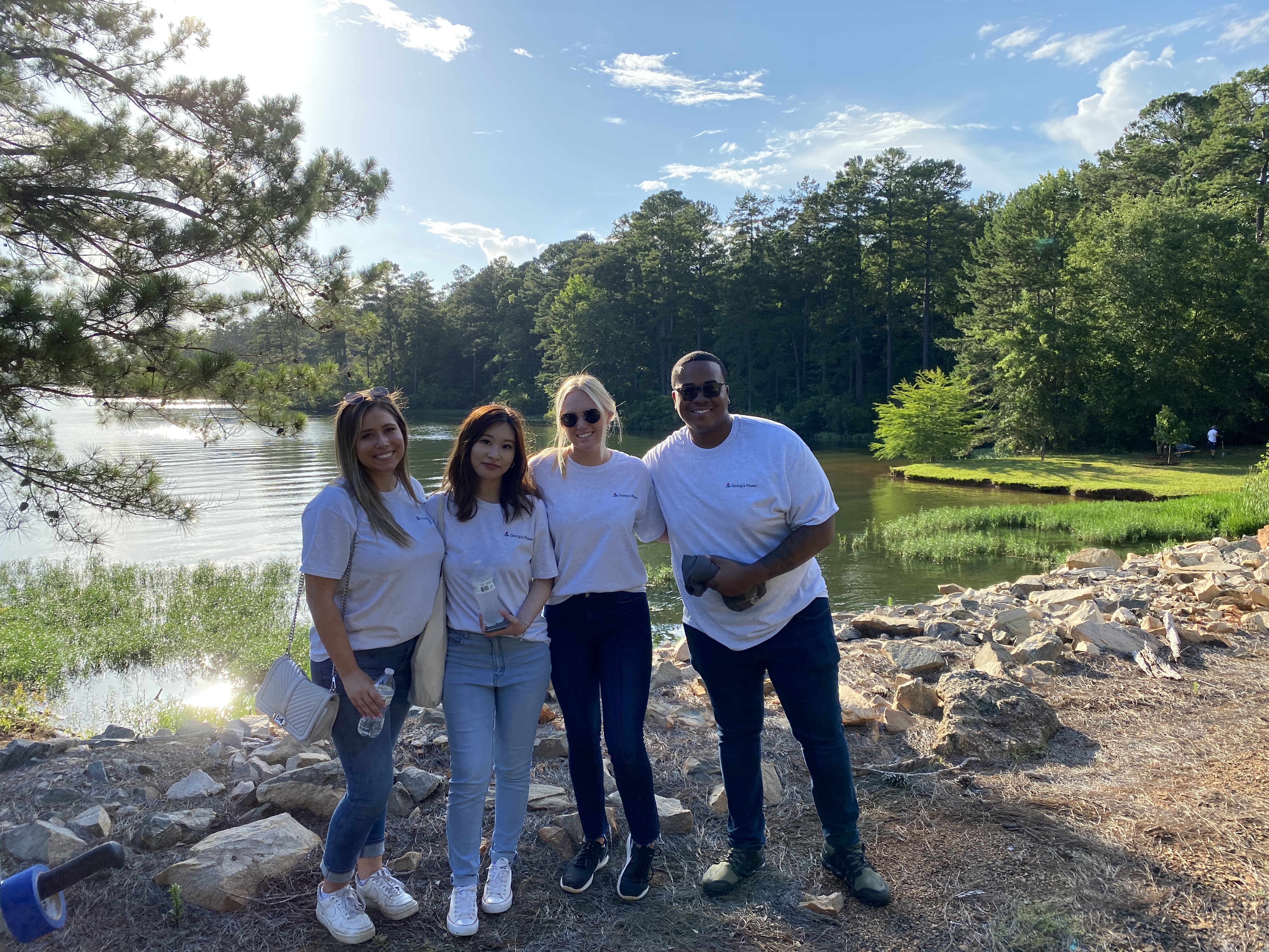 Drake and the other interns standing in front of a lake in white t-shirts under blue sunny skies