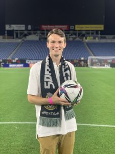 Hubbard holding a soccer ball and wearing a Soccer Club scarf in the stadium