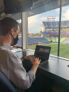 Hubbard typing on his laptop from a box overlooking the soccer stadium