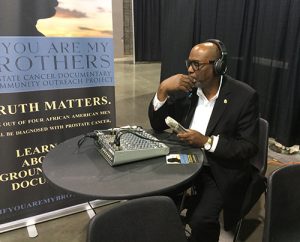 Reggie Hicks wearing headphones at a sound board as he promotes his documentary, You Are My Brothers.