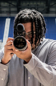 student LJ is holding up a camera while in the Red Bulls Soccer Club arena