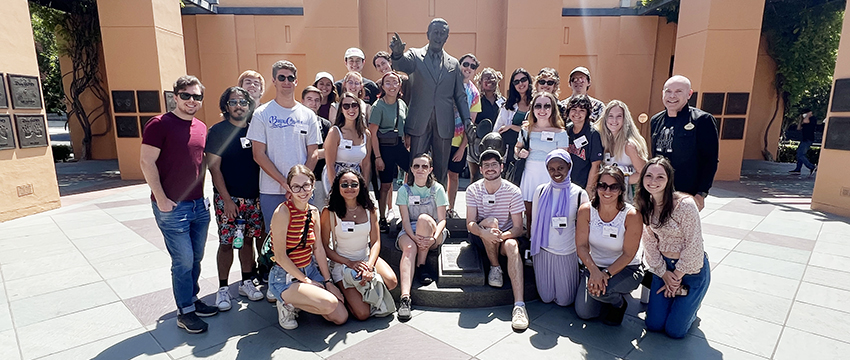 A group of students surrounds a statue of Walt Disney during a tour of D23, the Disney Fan Club.