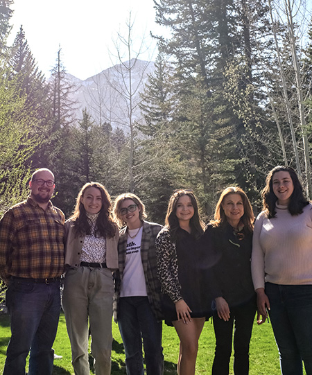 Four students and two faculty pose for a picture in Utah in front of a grove of trees with a mountain in the background. 