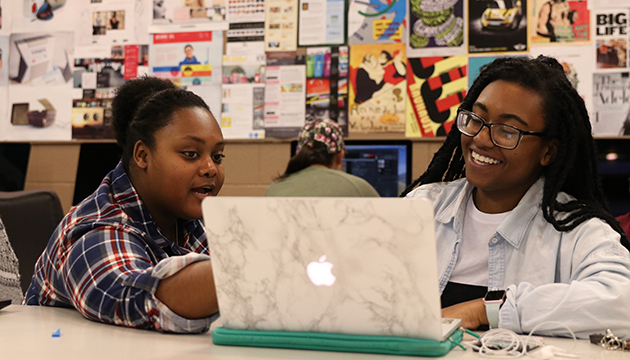 Two students laugh while looking at their computer.