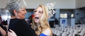 A beauty queen winner smiles broadly as she hugs a lady congratulating her.