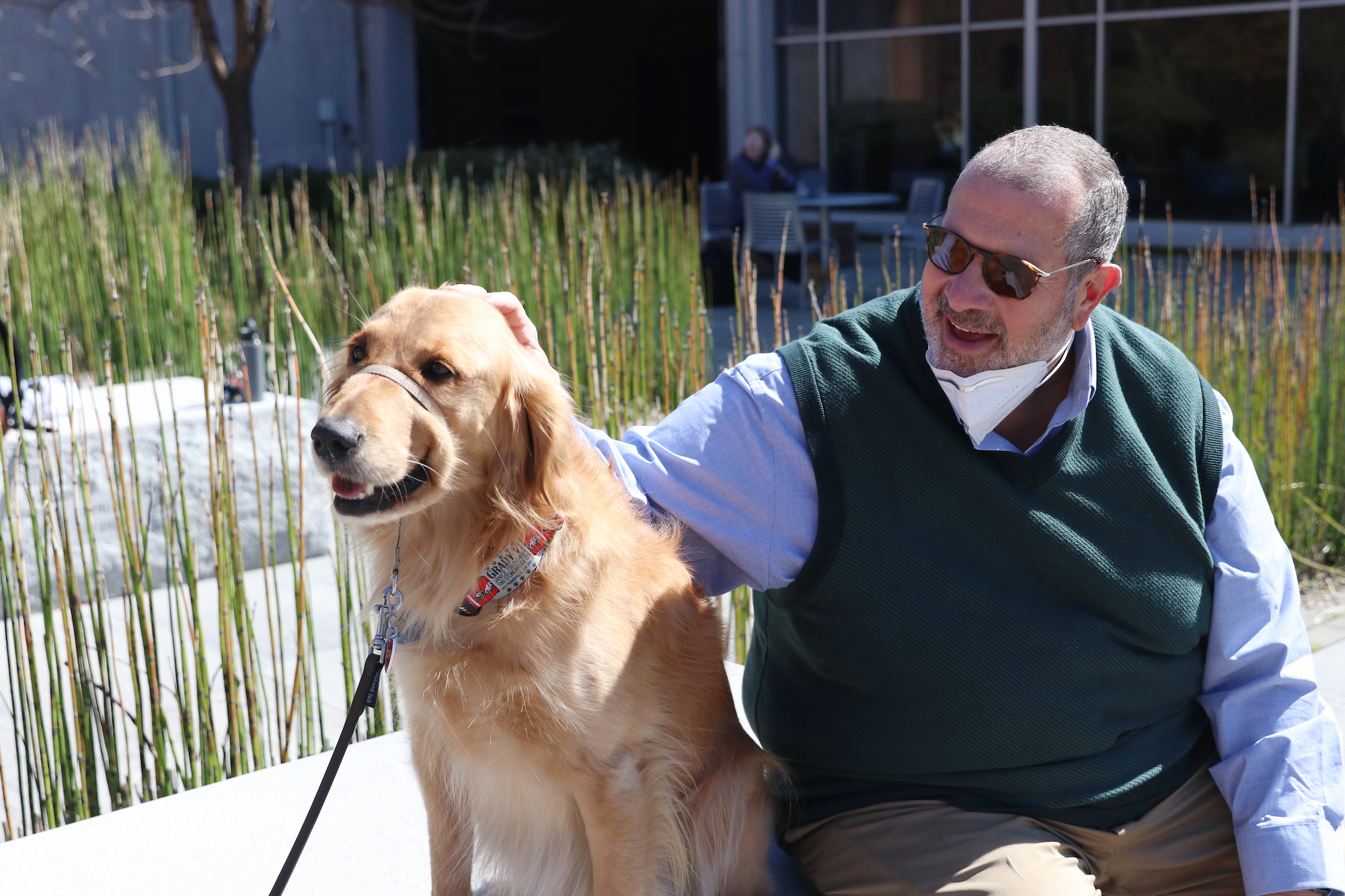 Dean Davos sits with a Golden Retriever on the Grady College lawn.