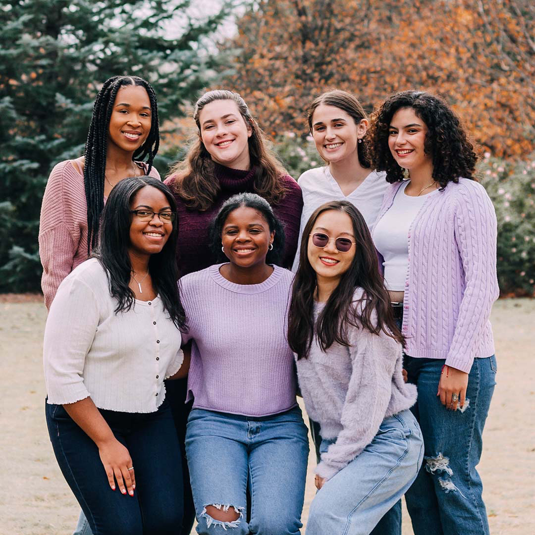 photo of seven female students wearing purple with a fall background