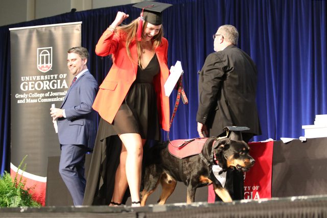 A graduate gives a fist pump as she and her dog cross the stage.