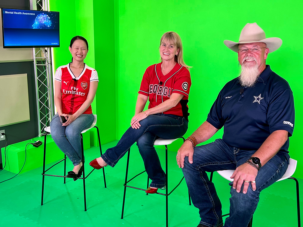Three people sit in front of a green screen in a production studio.