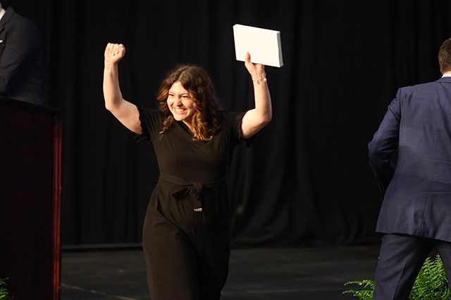 A student raises her arms in victory as she crosses the stage