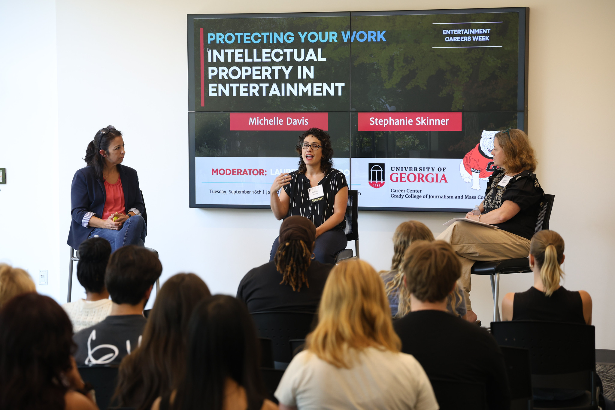 A panel discussion with a professor and two female alumni. In the background is a digital display that reads Intellectural Property in Entertainment.
