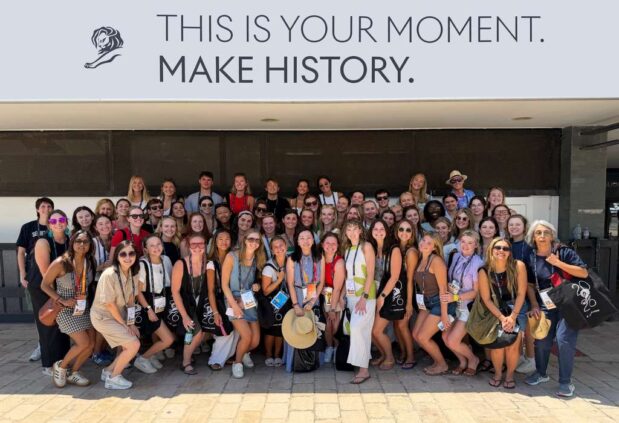 A large group of students pose for a picture under a banner that reads This is your moment, make history.