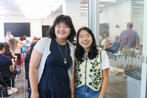 Two women pose for a picture in a busy room of people.