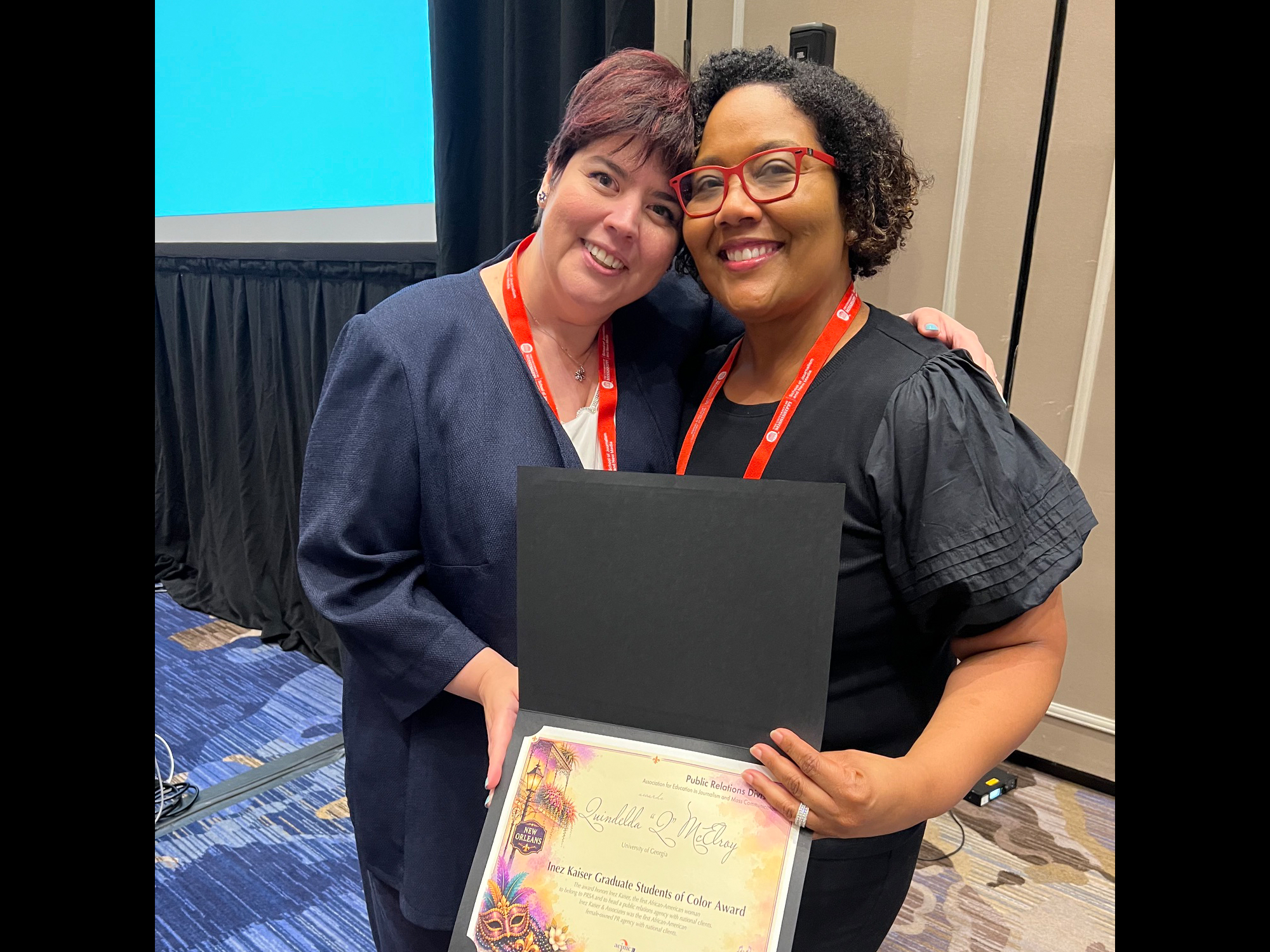 Q McElroy holds a certificate and receives a hug from another woman.