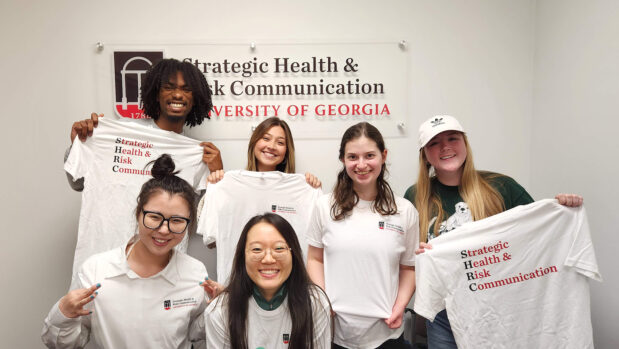 Students hold up tshirts in front of a Strategic Health and Risk Communication sign