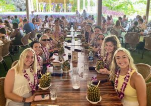 Group of students on the Travel Writing in Hawaii Study Away program. Students are wearing a lei and drinking from pineapples at a dinner.