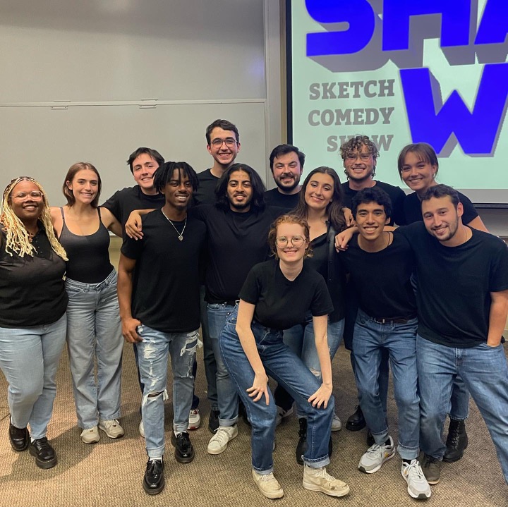 Dani Garcia Pozo and students stand in front of a Shark Sketch Comedy screen.