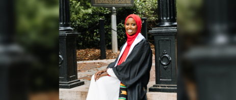 Fardosa Hassan in her graduation gown, sits at the UGA Arch.