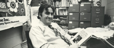 John English holds a book at a desk in an office around 1984.
