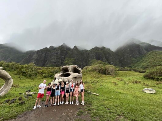 Students on the Hawaii study away program stand in front of a giant faux dinosaur skeleton from the set of the movie The Jurassic Park.