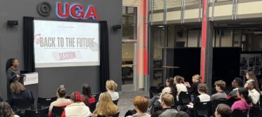 Media literacy influencer Kelsey Russell stands at the front of Studio 100, presenting to a group of students seated in front of her. Her presentation projected behind her reads "Back to the Future."