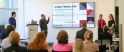 Students stand in front of a display and present their research.