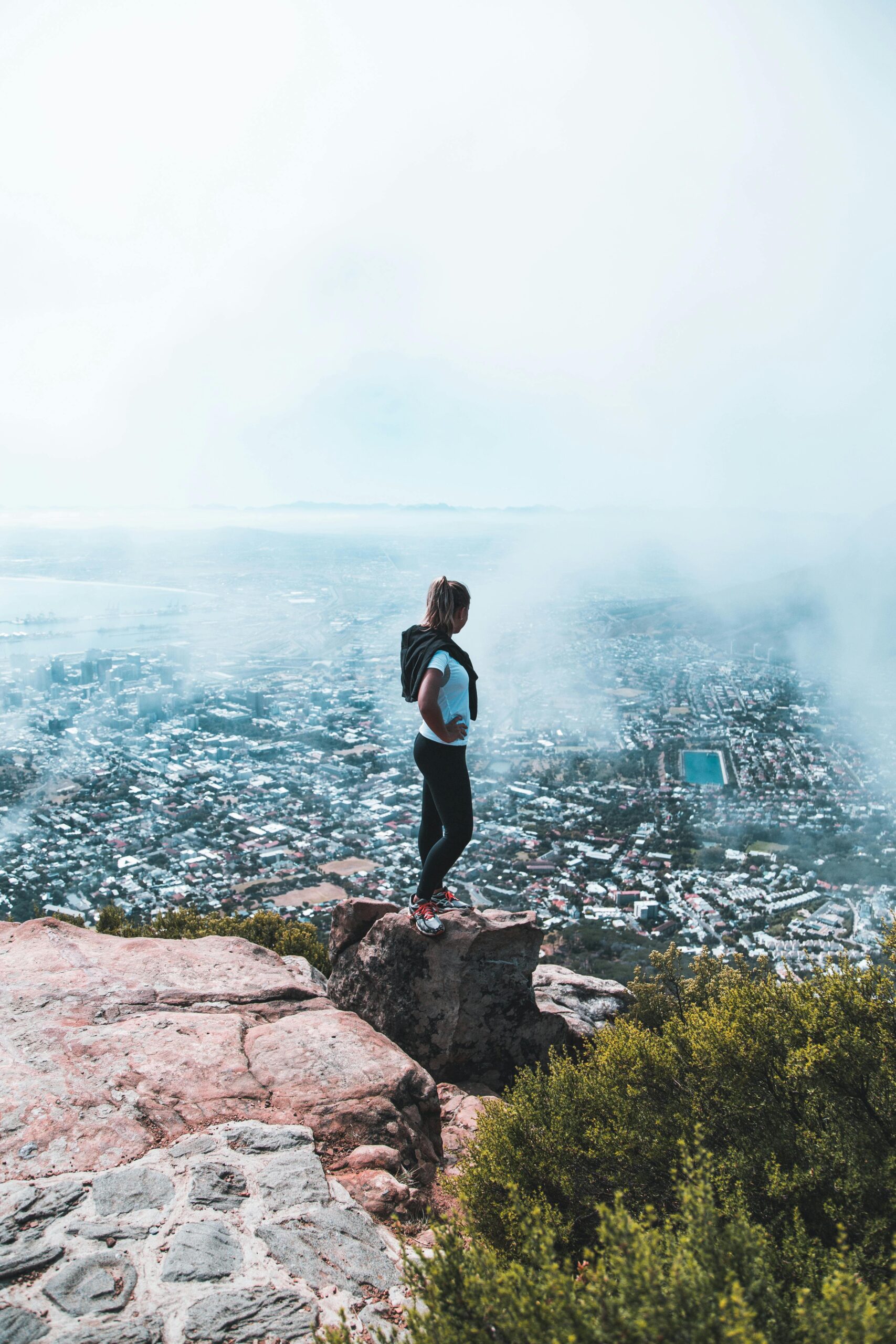 Woman stands on top of a mountain overlooking Cape Town, South Africa.