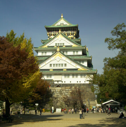 Osaka Castle in Japan with trees and people in the foreground.