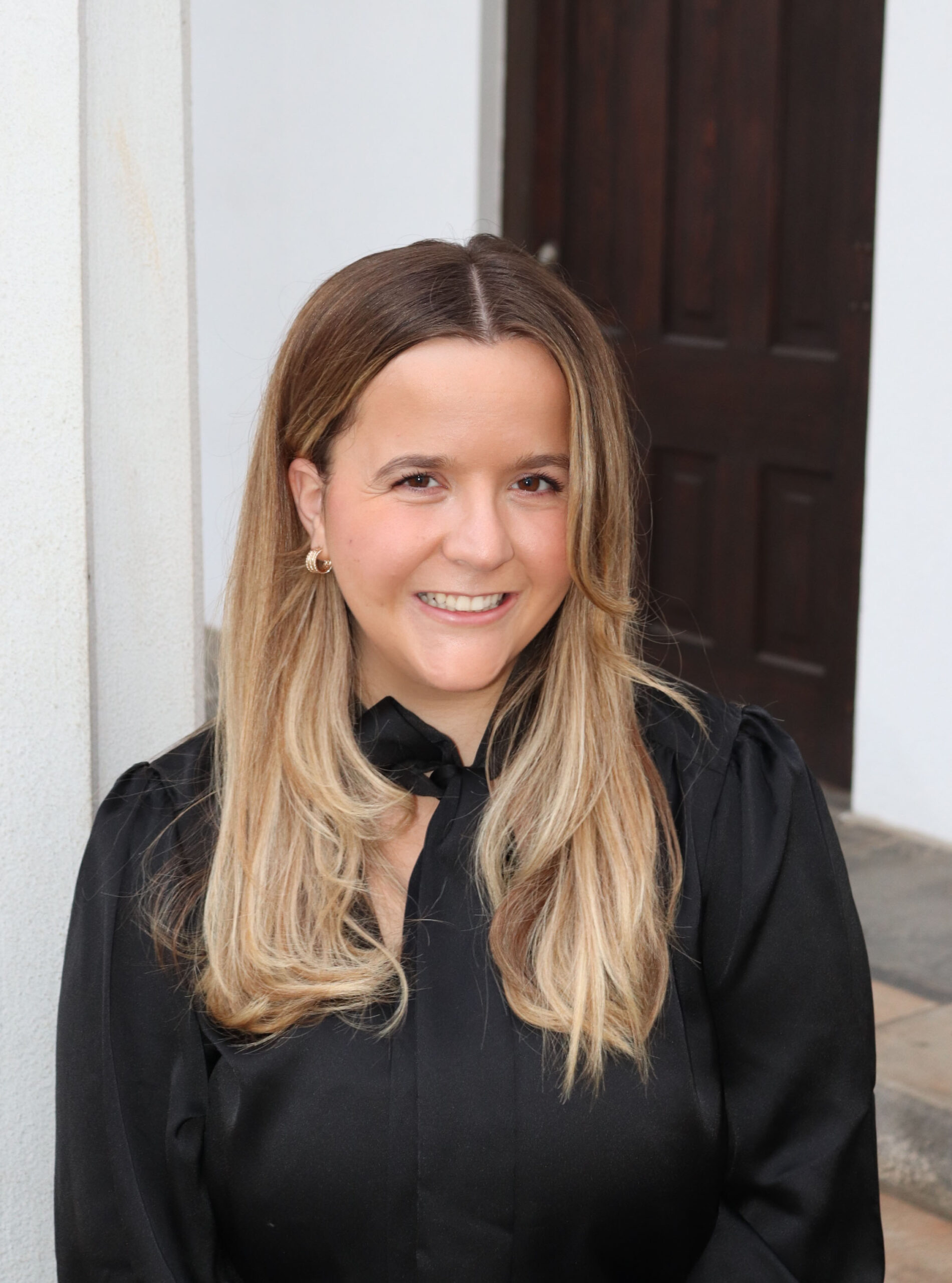 Photograph of AdPR Connection Co-Director Hannah WIlliams standing in front of a white building with a brown door.