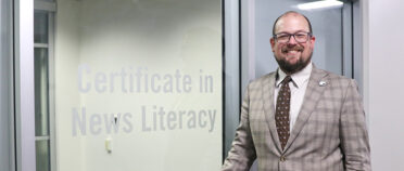 Headshot of Kyser Lough in front of a sign that reads "Certificate in News Literacy."