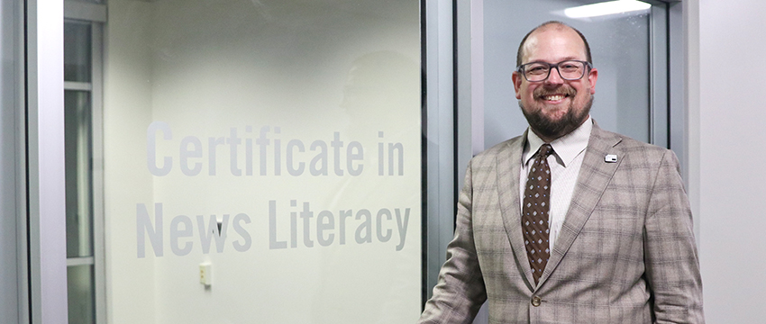 Headshot of Kyser Lough in front of a sign that reads "Certificate in News Literacy."