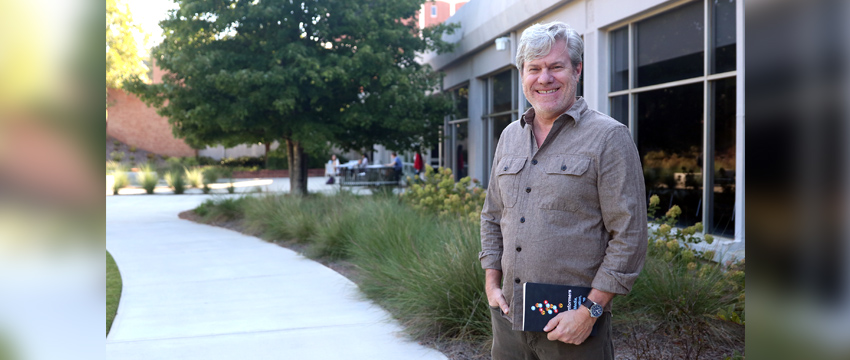 Lance Porter stands in front of Grady College with his new book in his hand.