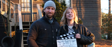 Man and woman in front of a house with a film slate.