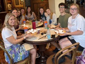 A group of students sit with their professor at a Disney restaurant eating Beignets together. 