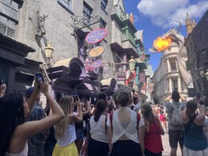 A group of people explore that Wizarding World of Harry Potter's Diagon Alley in Orlando, Florida. There is a large dragon breathing fire that everyone seems to have their eyes drawn towards.