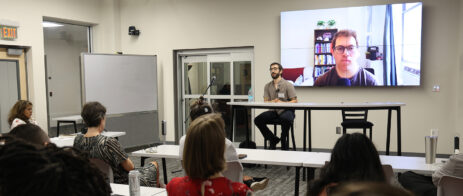 Max Blau sits facing a group of MFA students as a screen in the background shows Jacob Feldman.
