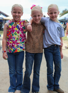Three triplets smile and have their arms around one another at the fair.