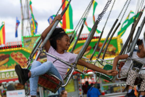 A girl reaches out for the hand of the girl next to hear as she enjoys a swing ride at the fair.