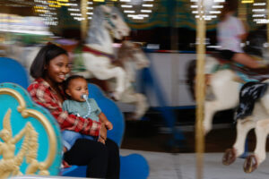 A woman and toddler on her life enjoy the merry-go-round at the fair.