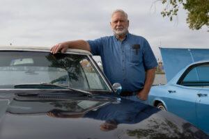 A man rests his arm on the top of his classic car at the fair.