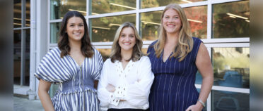 Three women pose for a portrait outside the Grady College building.