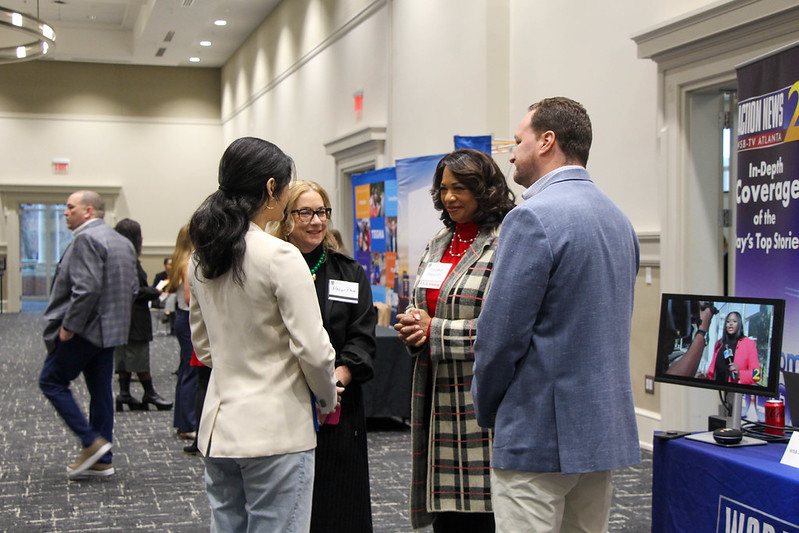 Group of professionals stand up and talk to one another during career fair.