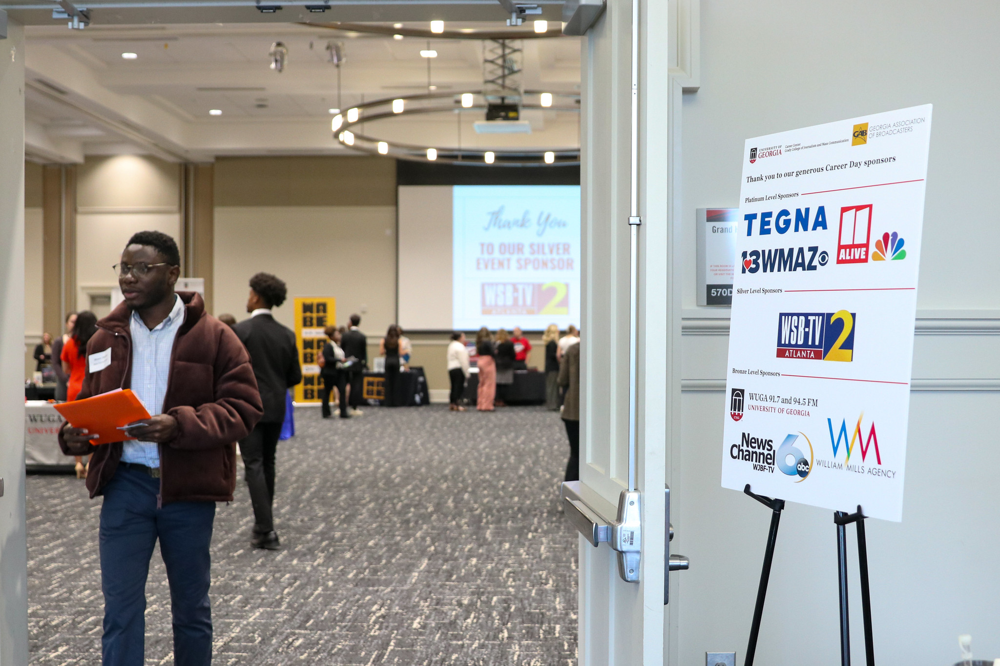 Student exits the career fair through doors. A sign with sponsor logos is on an easel to the right.