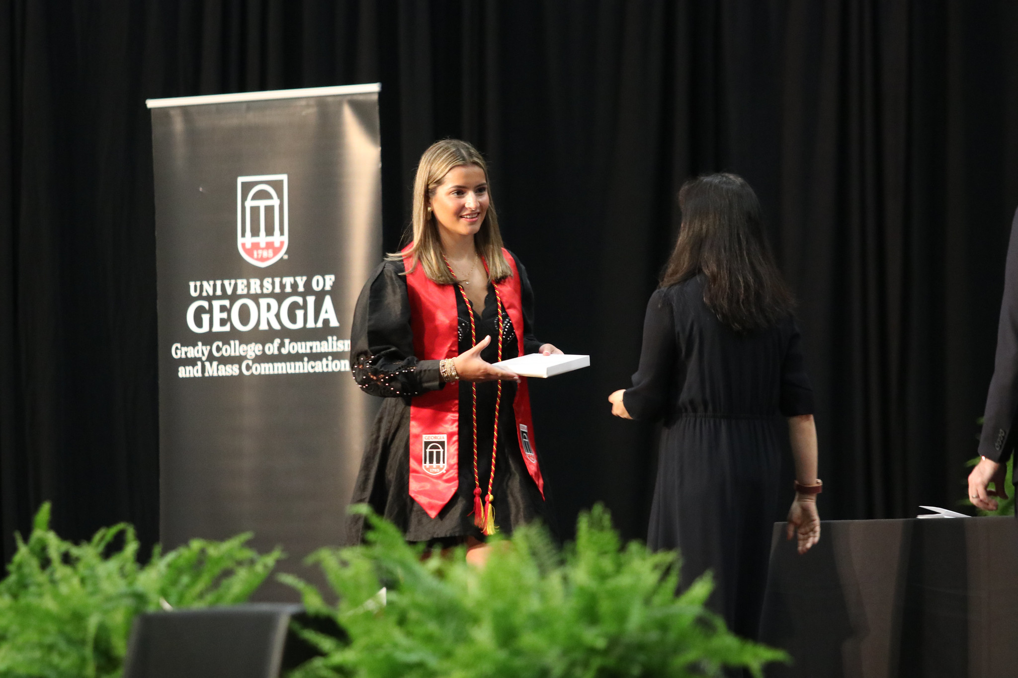 A girl with a graduation stole smiles as she crosses the stage.