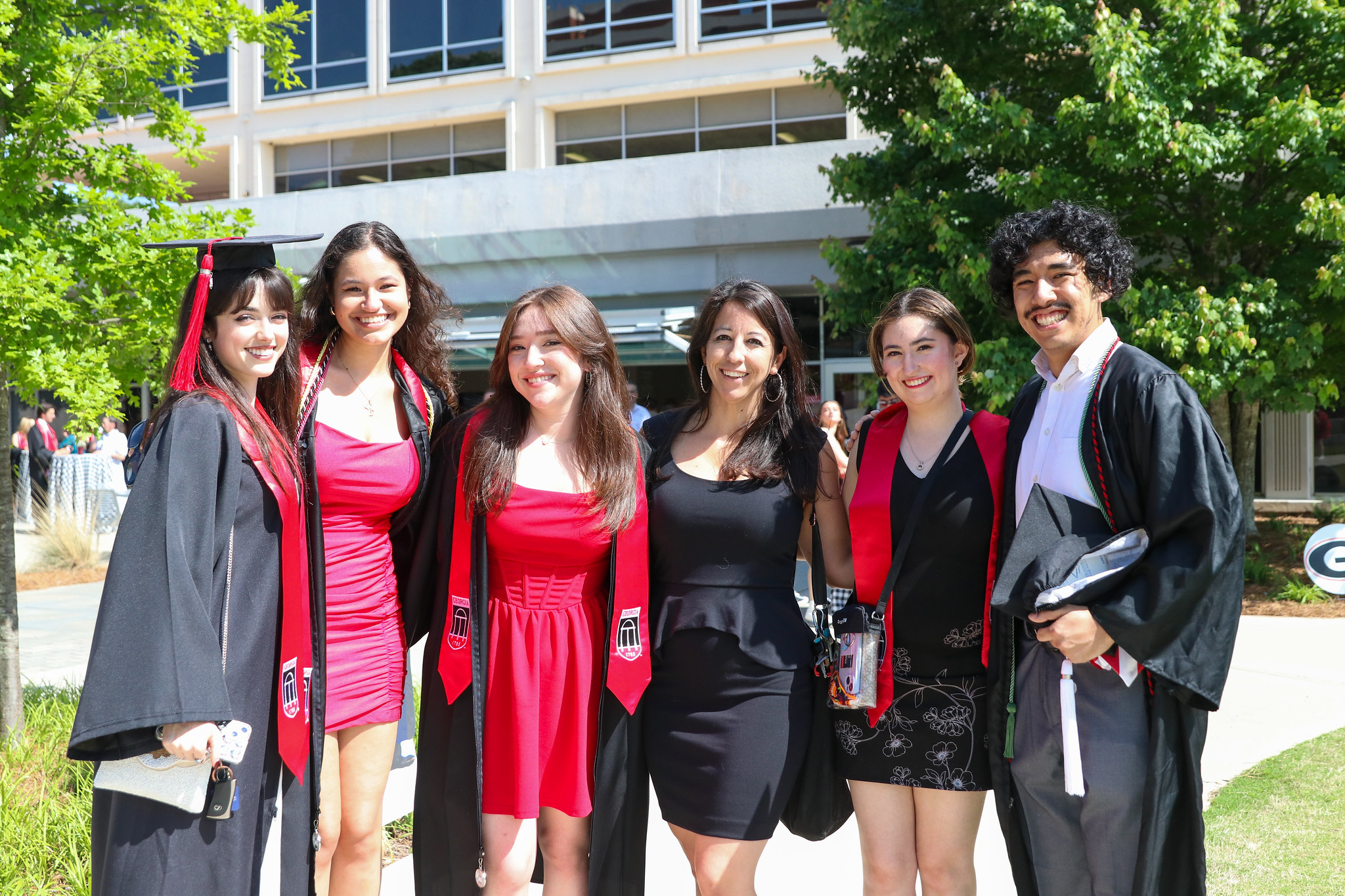 A professor and students with graduation gowns and stoles pose for a picture in front of Grady College.