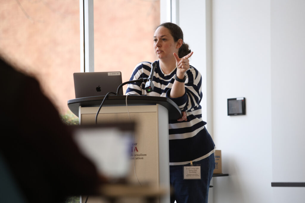 A woman makes a gesture while standing at a lectern.