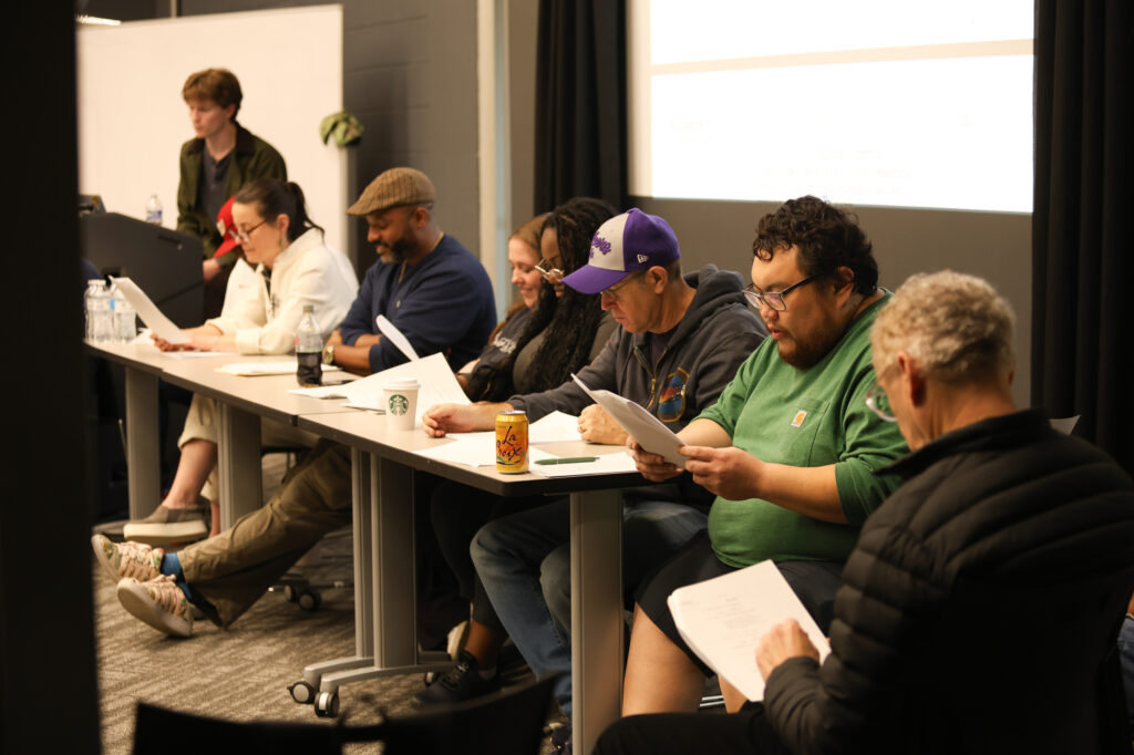 Several people sit at a table and read a script.