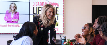 Deborah Norville smiles as she leans across a table and talks with students.