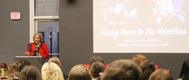 Charlayne Hunter Gault speaks in front of a group of students with a screen in the background that reads "Giving Voice to the Voiceless."